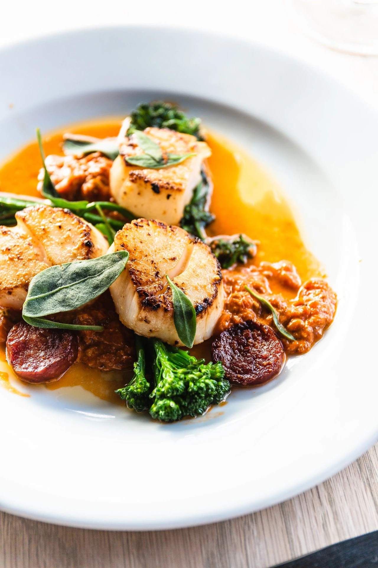 Seared scallops with colorful vegetables, herbs and orange sauce on a white plate.