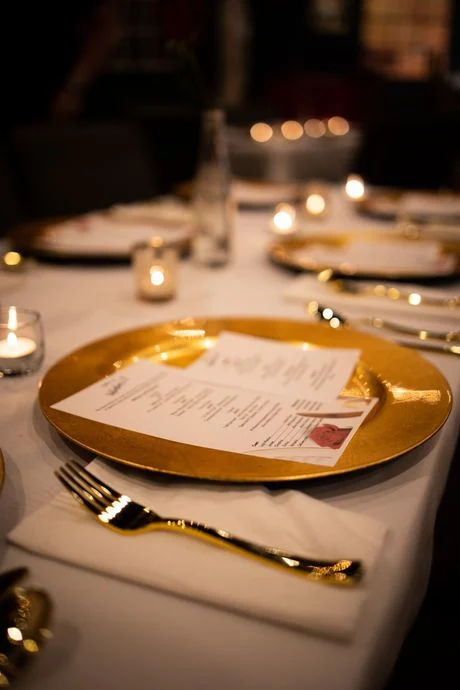 A printed menu on a gold charger at a candlelit dinner place setting.