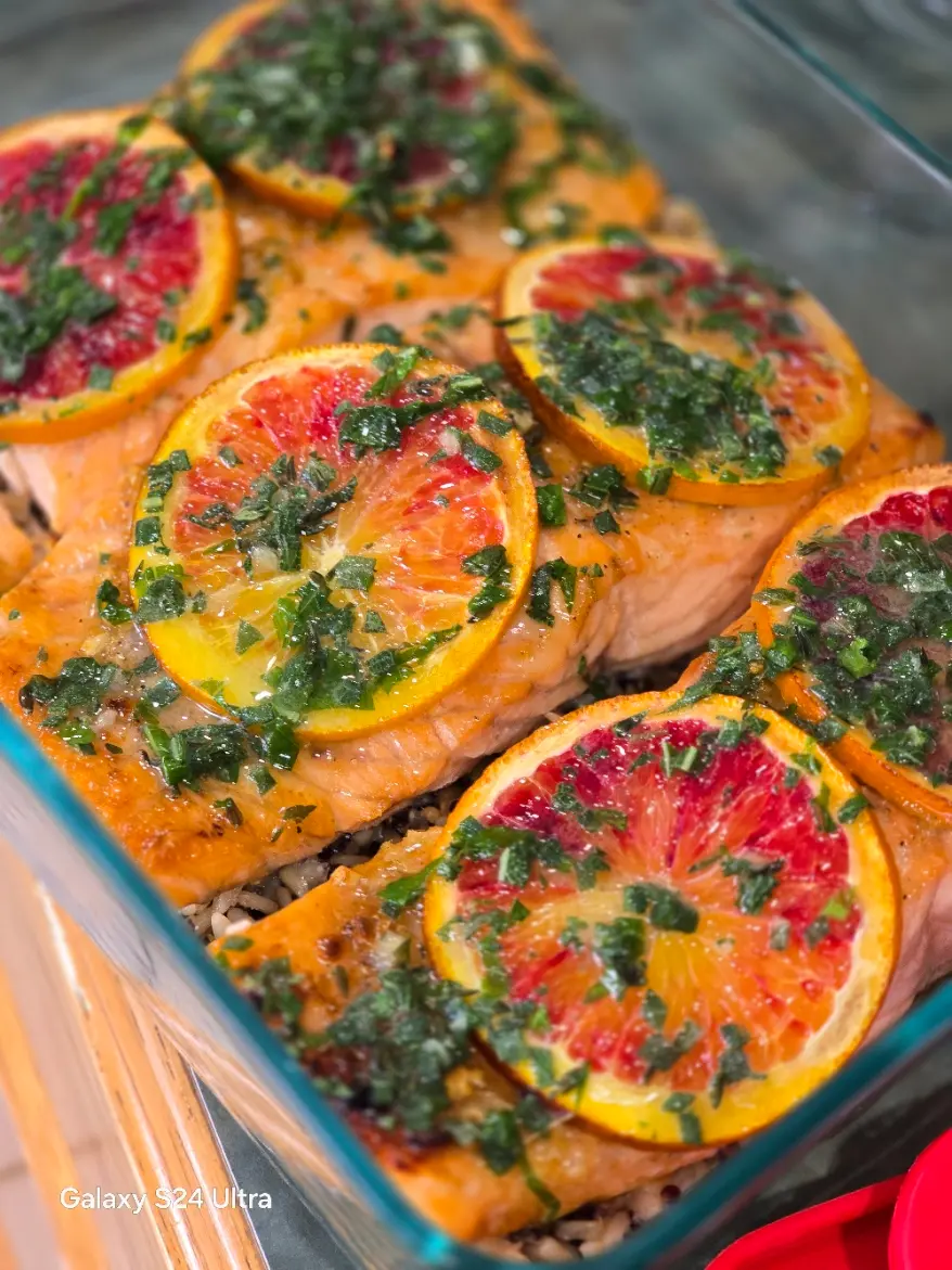 Salmon portions topped with citrus slices and chopped herbs in a roasting dish.