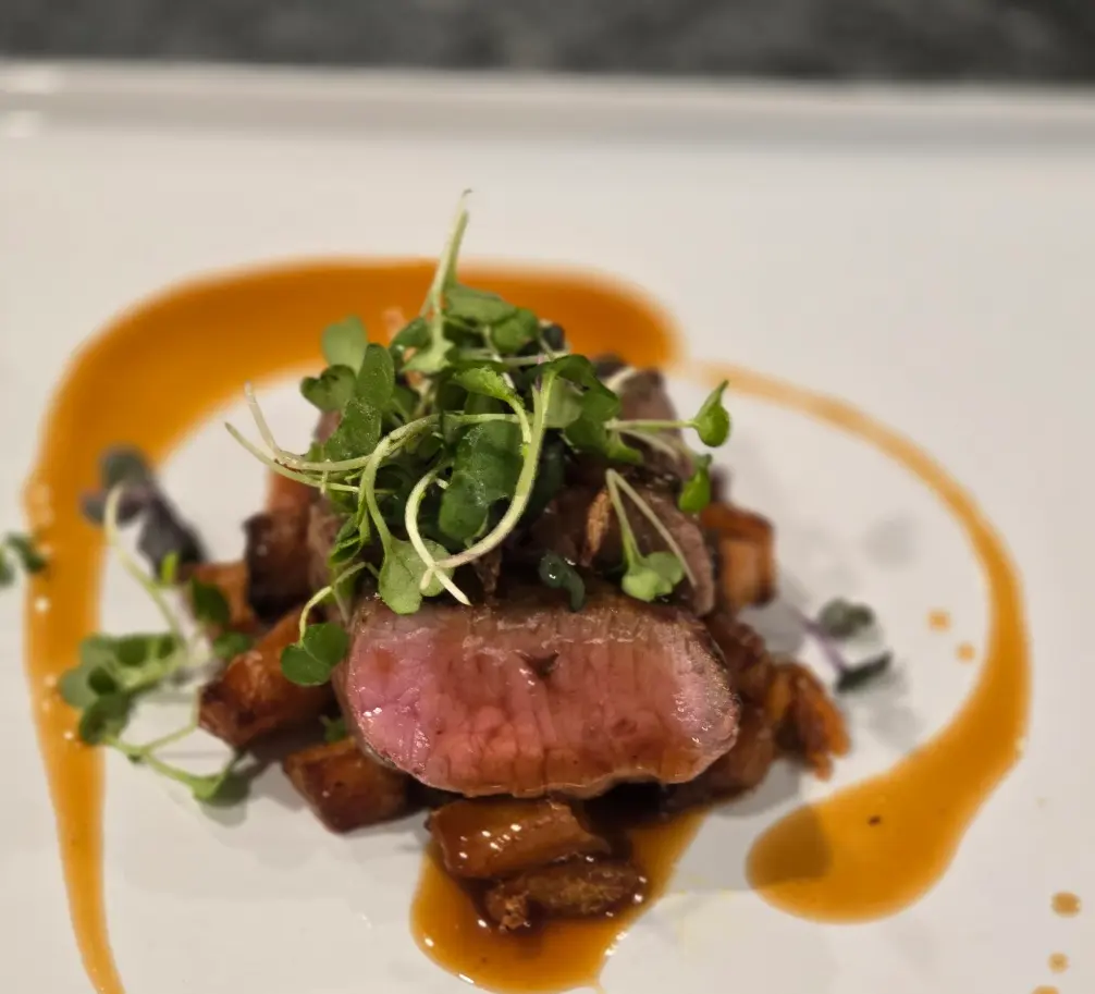 Sliced Brandt beef topped with microgreens and surrounded by a swirl of sauce.