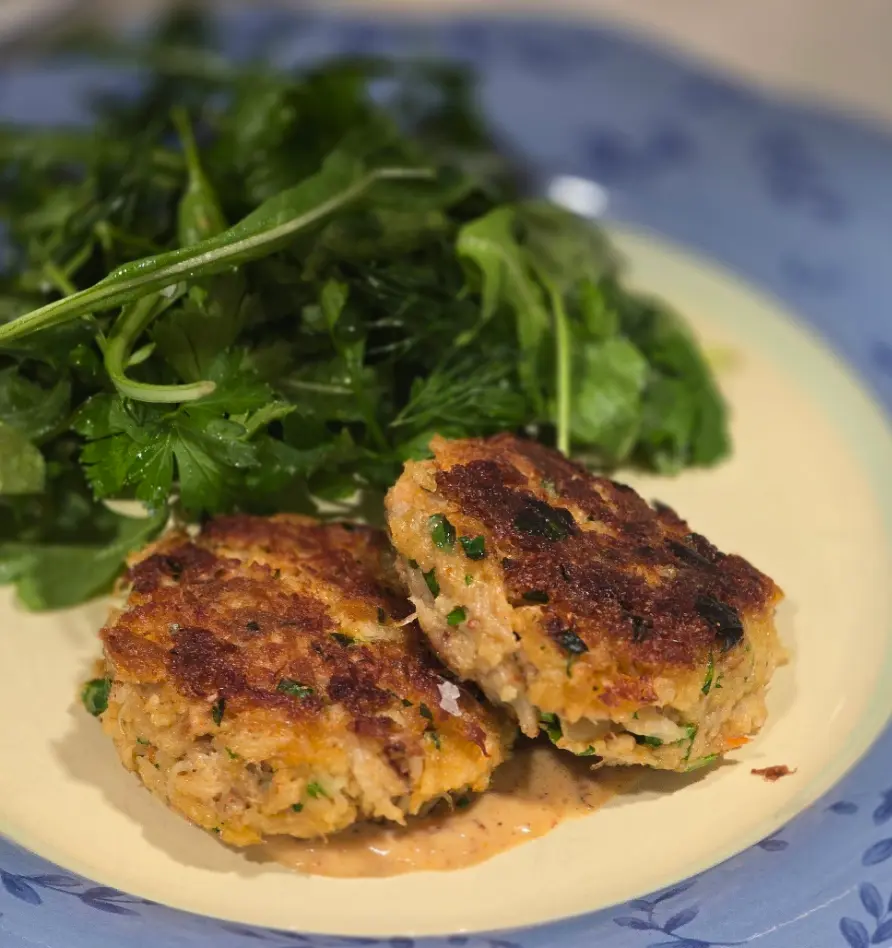 Two golden crab cakes with Cajun remoulade and leafy greens.