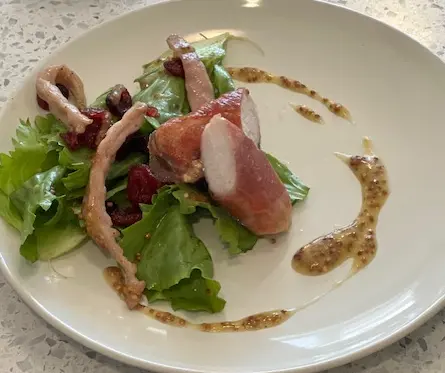 Sliced rabbit loin served with leafy greens, radishes and a grainy sauce.