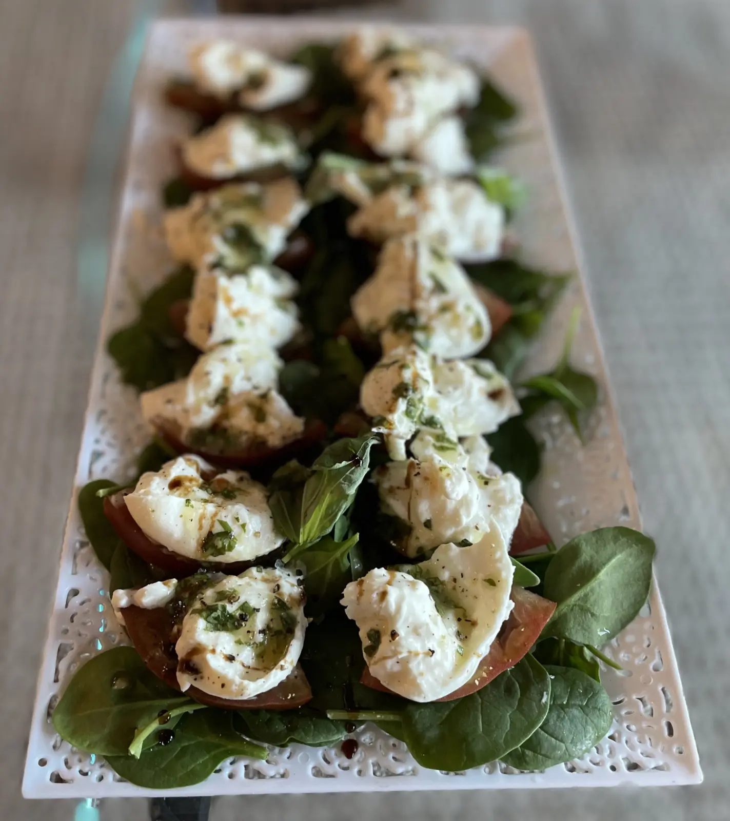 Heirloom tomato and burrata salad with leafy greens on a long serving platter.