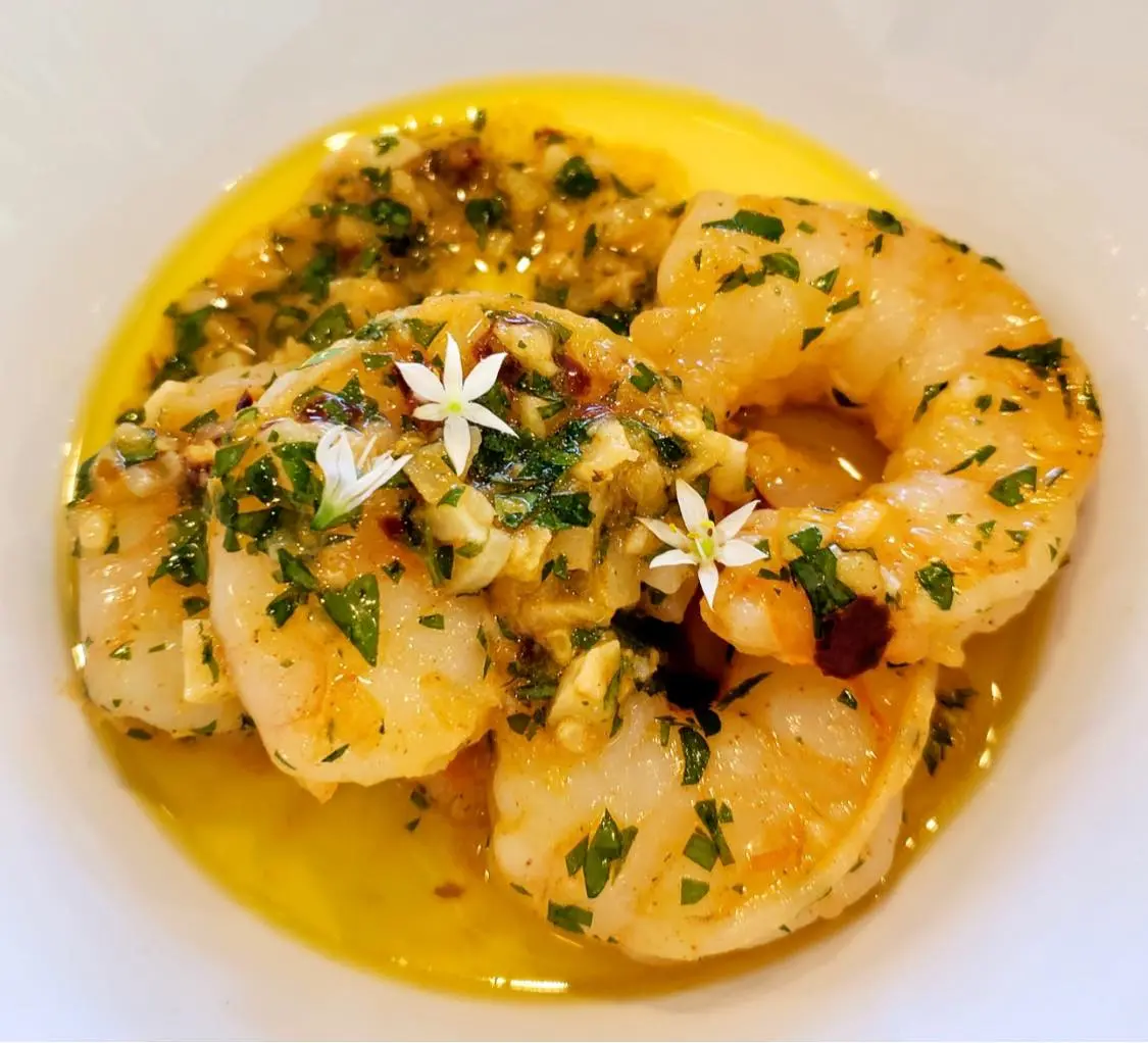Gambas al ajillo with shrimp, sliced garlic, herbs and small edible flowers.