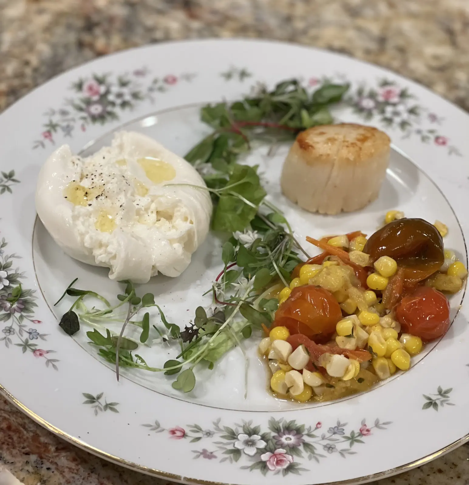 A brown butter scallop plated with creamy cheese, tomatoes, corn and greens.