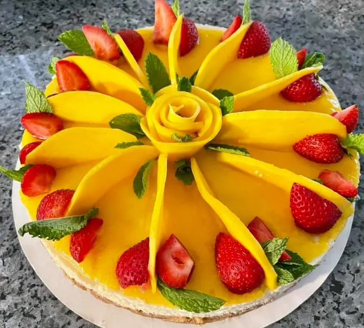Mango cheesecake decorated with fanned mango slices, strawberries and mint.