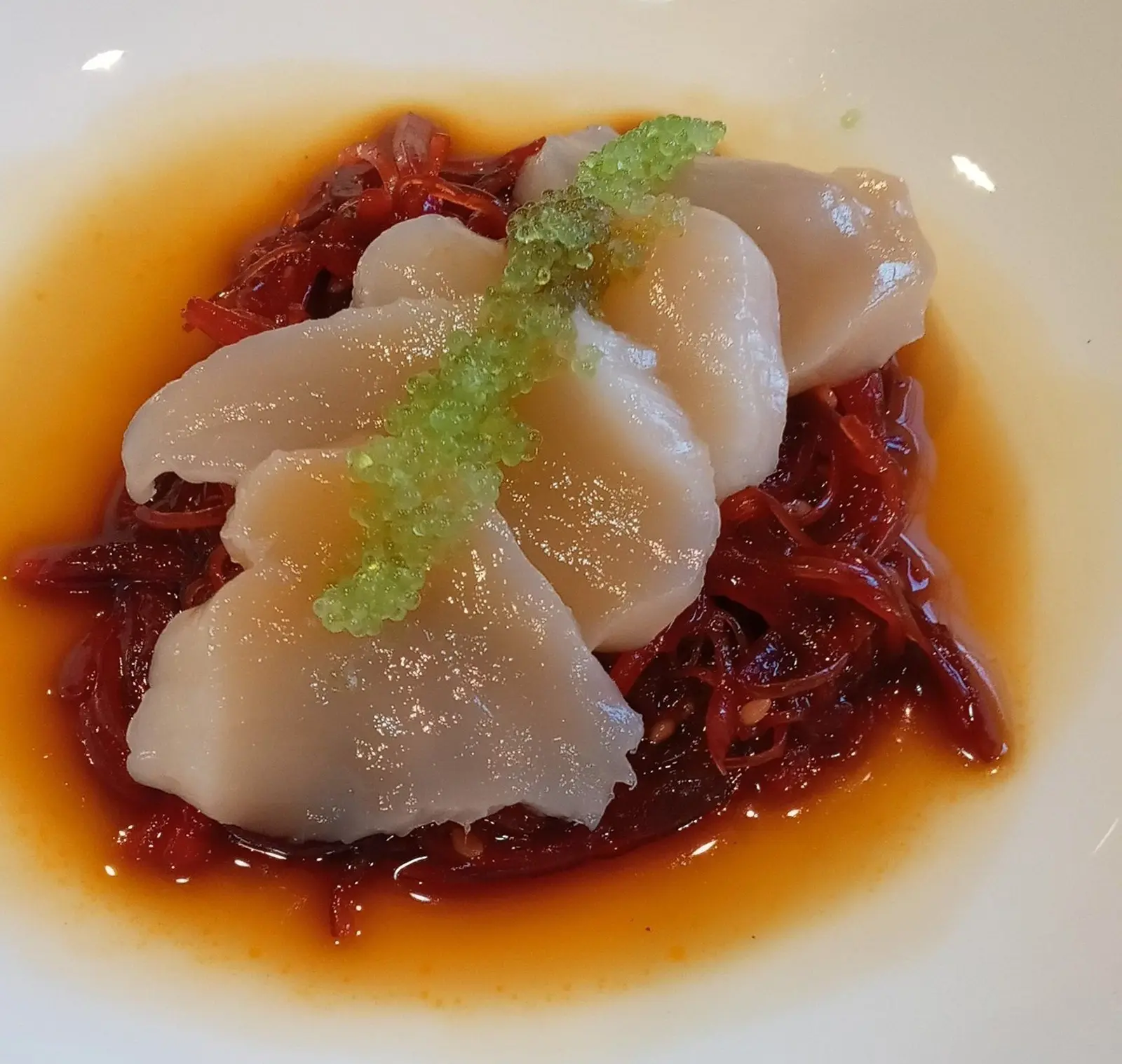 Thinly sliced sashimi scallops with green garnish over red sauce.