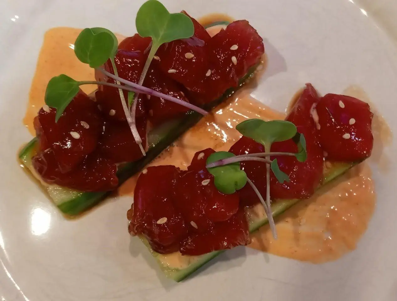 Ahi tuna bites on cucumber with a red topping, sesame seeds and microgreens.