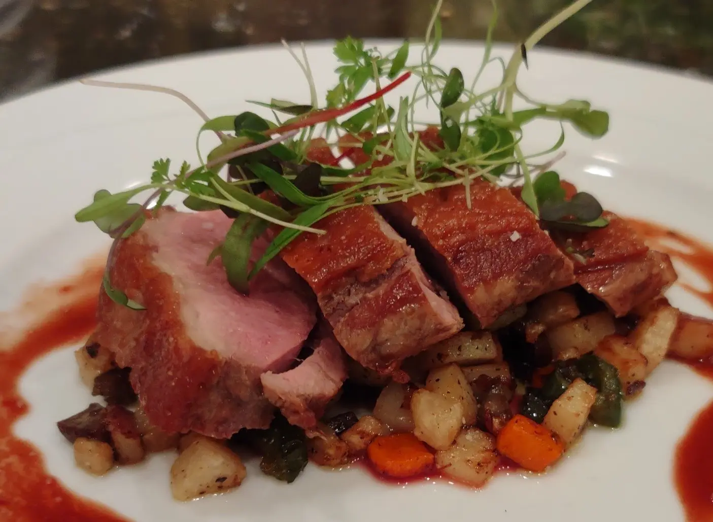 Sliced pan-seared duck breast over diced vegetables with fresh microgreens.