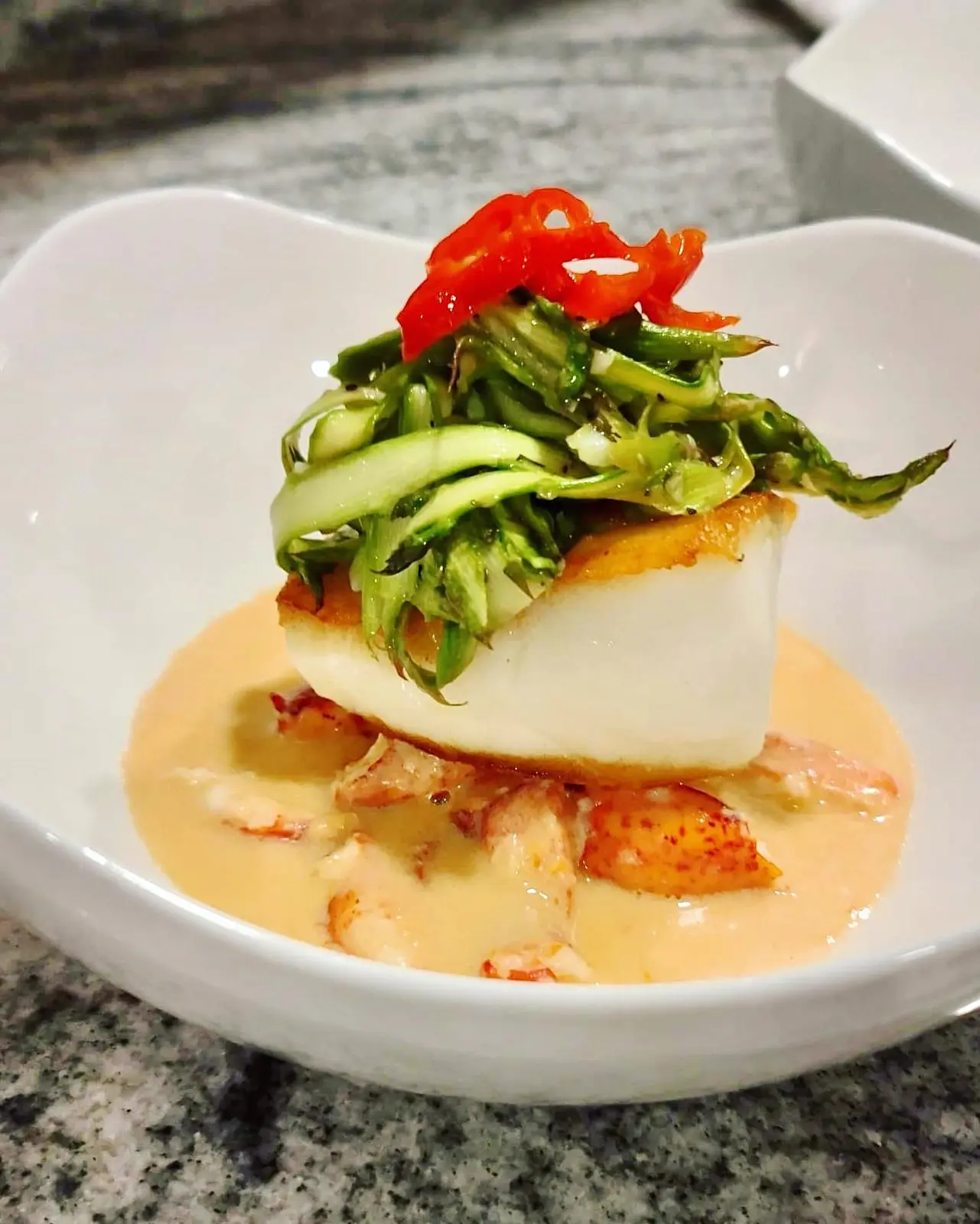 Seared striped sea bass with green vegetables, red peppers and pale sauce.