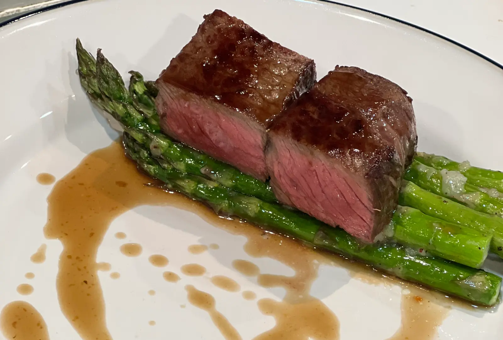 Two pieces of pan-seared Piedmontese beef resting on asparagus spears.