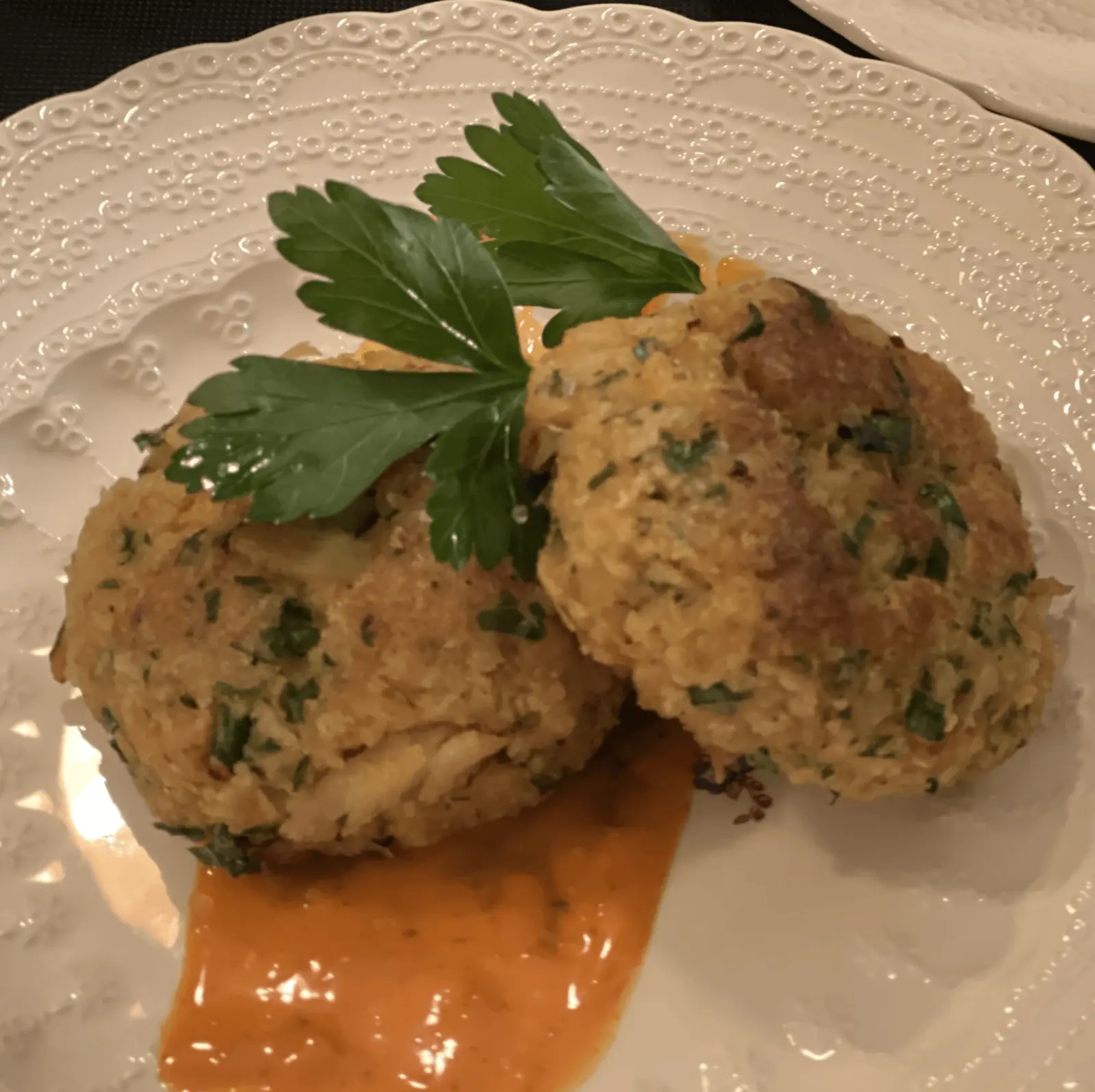 Jumbo lump crab cakes with a pale orange sauce and parsley garnish.