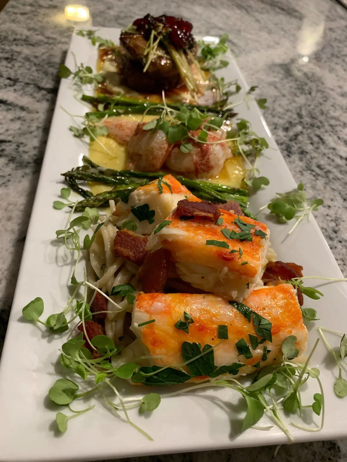 A premium appetizer trio arranged with fresh herbs on a long white plate.