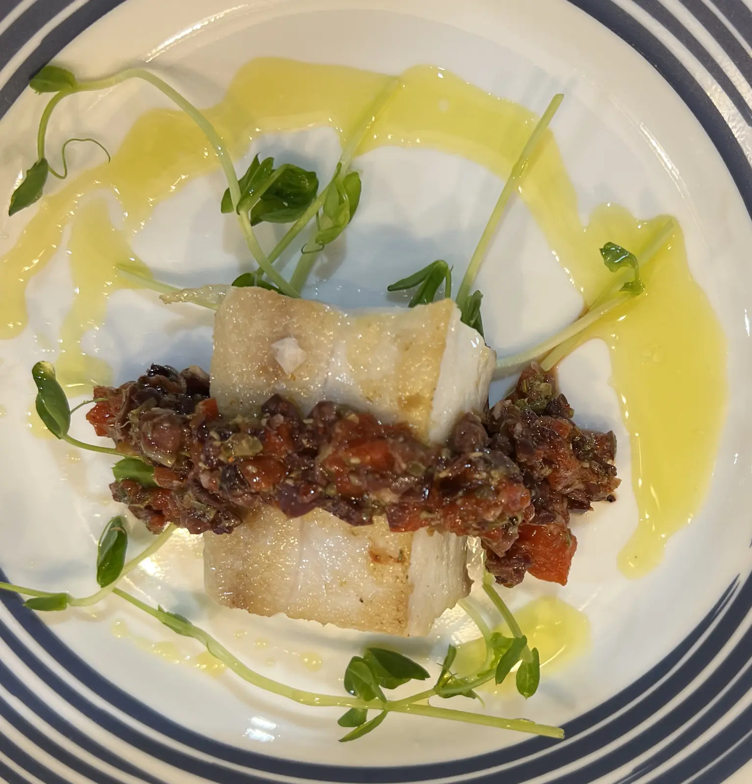 Mahi-mahi topped with a chopped garnish and surrounded by green oil and microgreens.