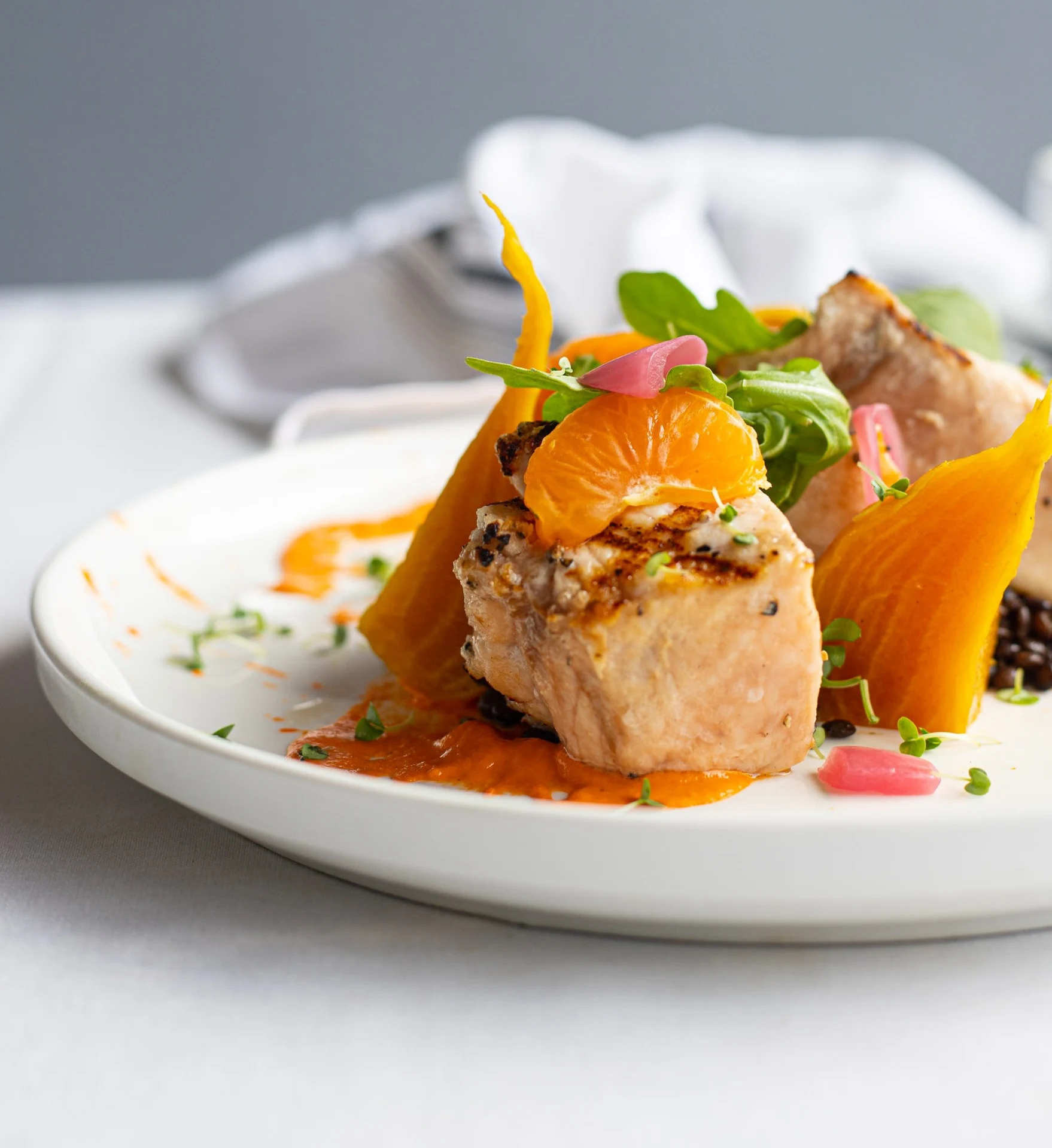 An individually plated entree with colorful vegetables, herbs and orange sauce.