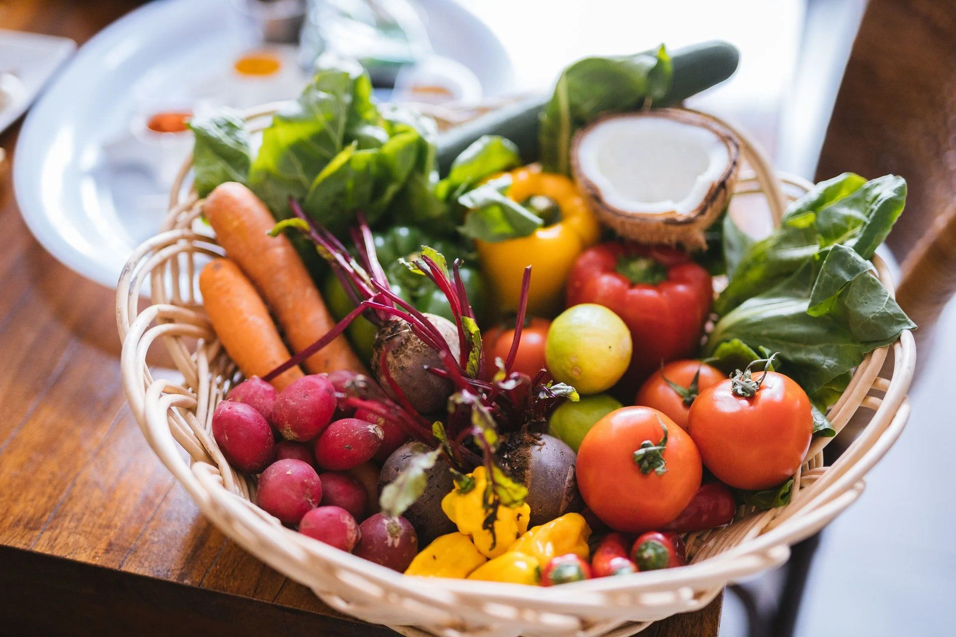 A basket of fresh carrots, radishes, peppers, tomatoes and leafy greens.