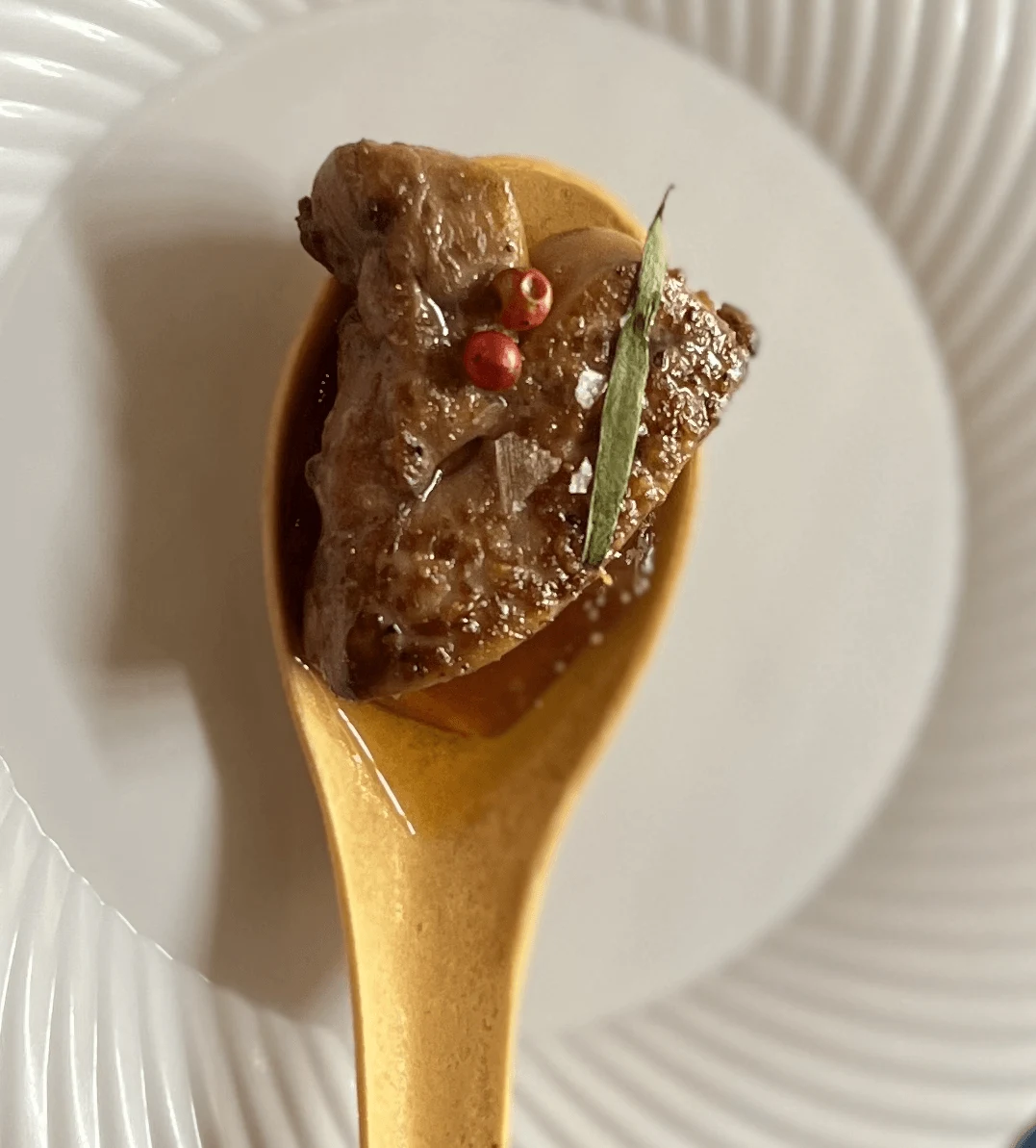 A foie gras amuse-bouche presented on a wooden tasting spoon.