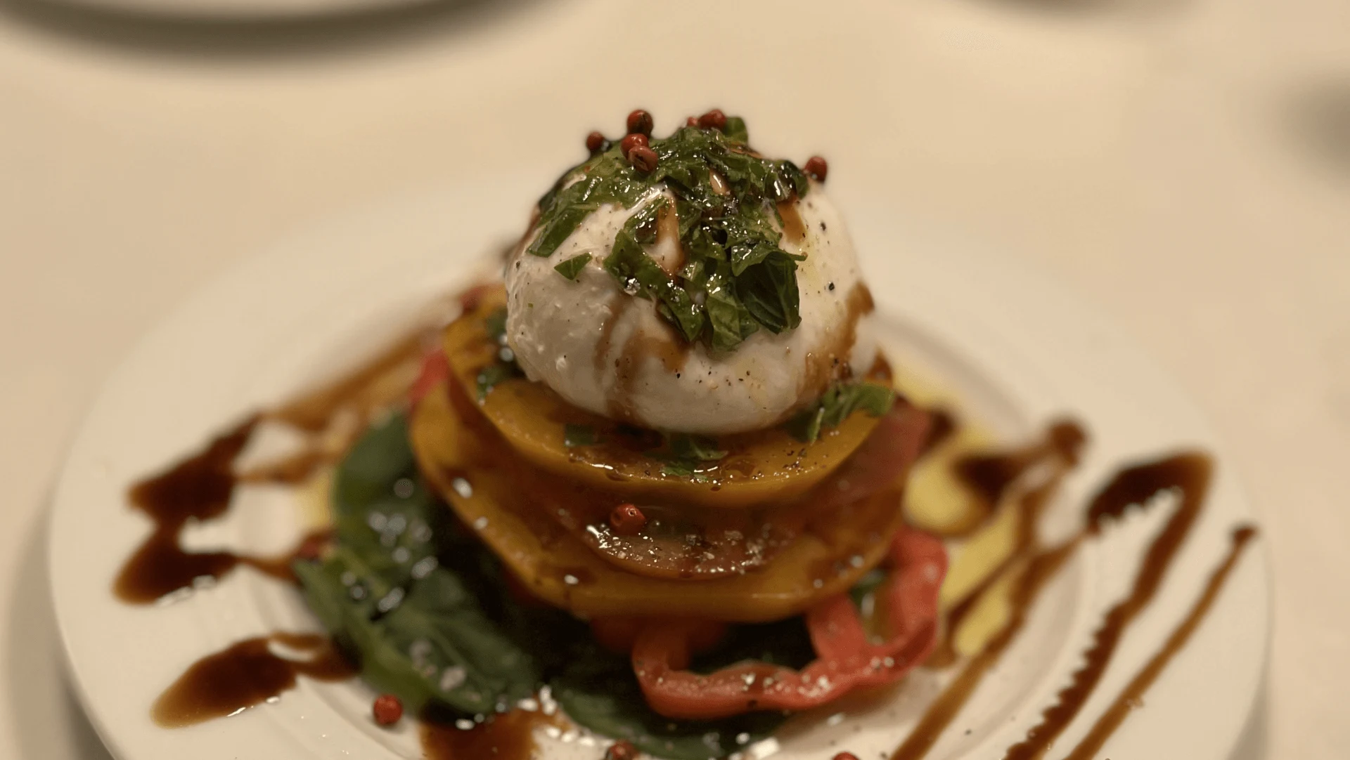 Burrata atop layered heirloom tomatoes with herbs and balsamic drizzle.