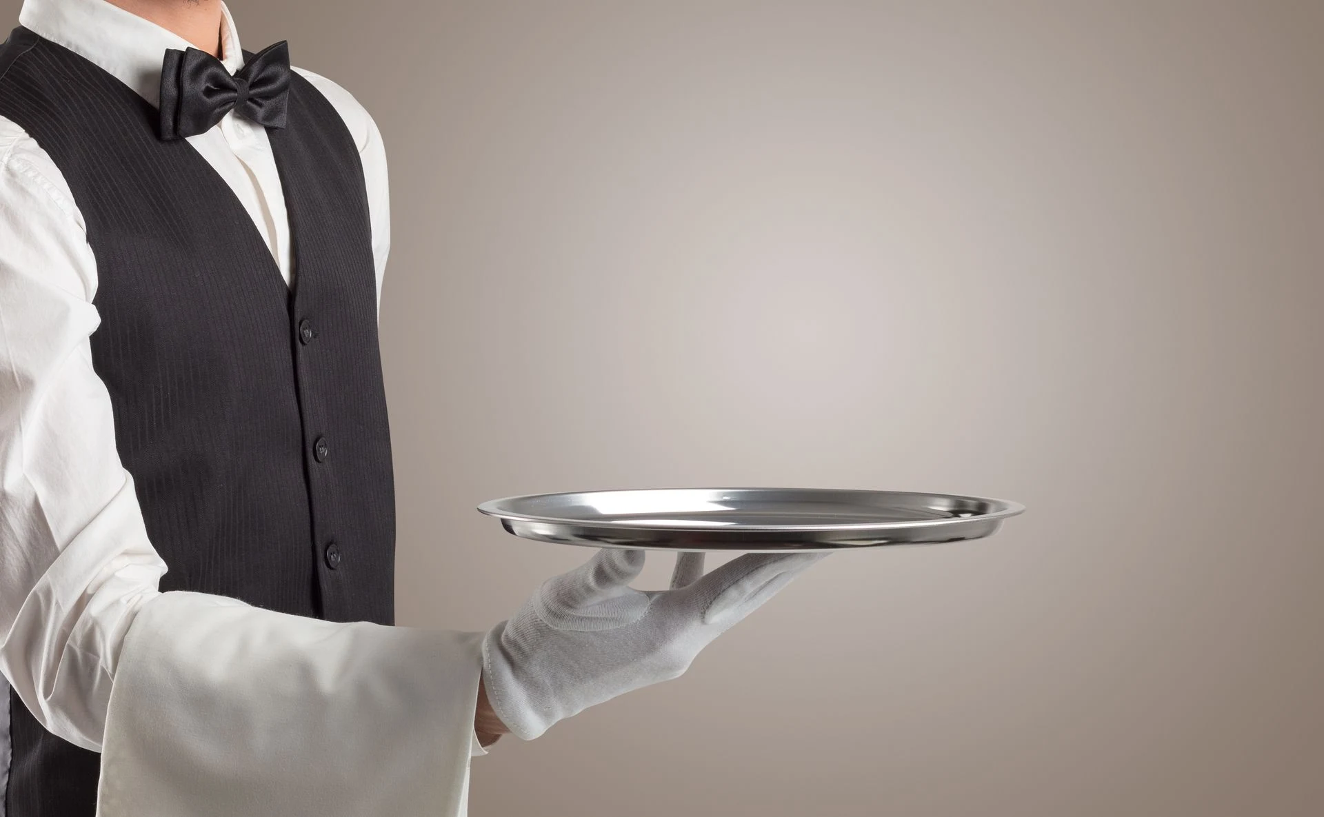 A steward in formal service attire holding a silver serving tray.