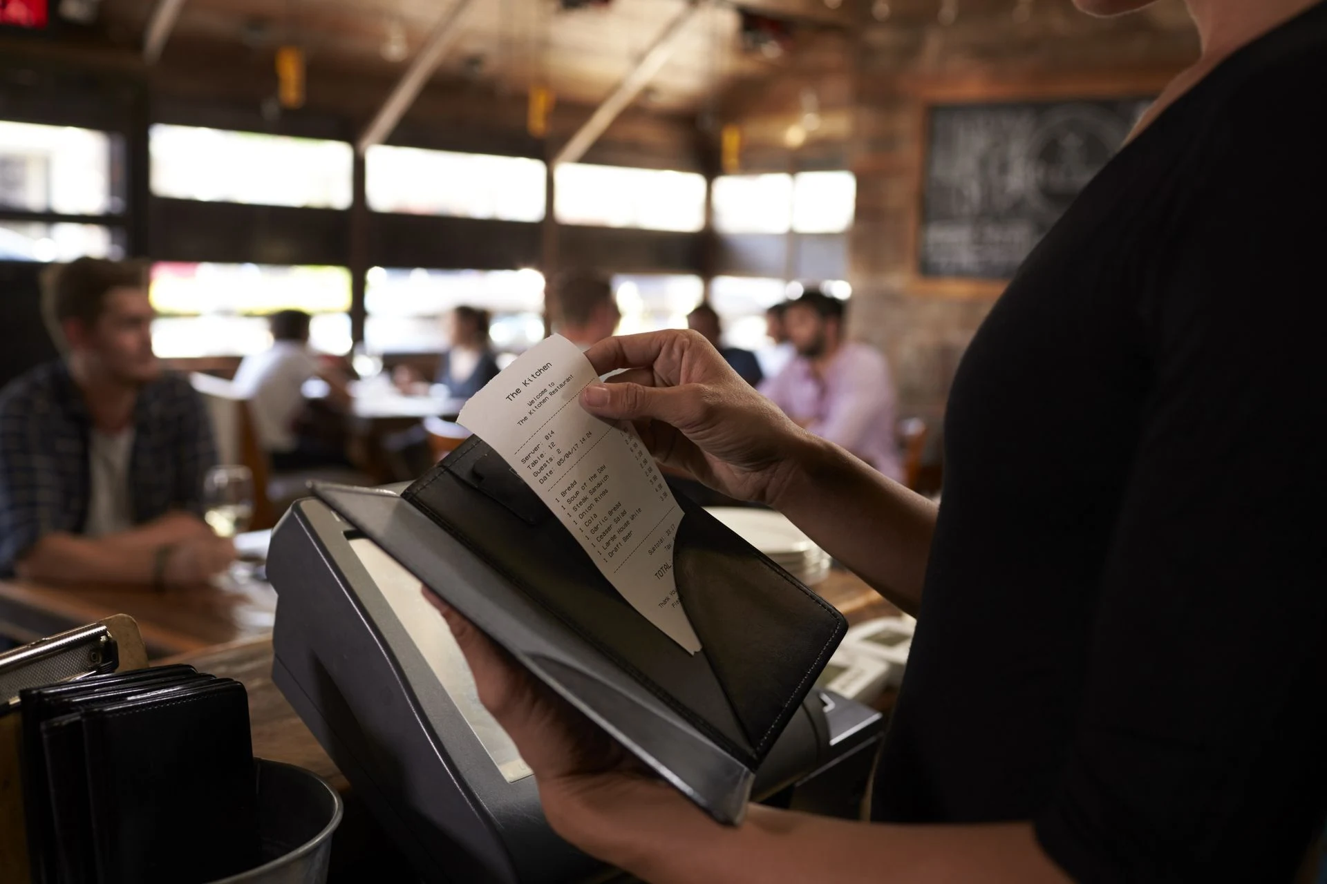 A restaurant guest reviewing a printed bill beside a payment terminal.