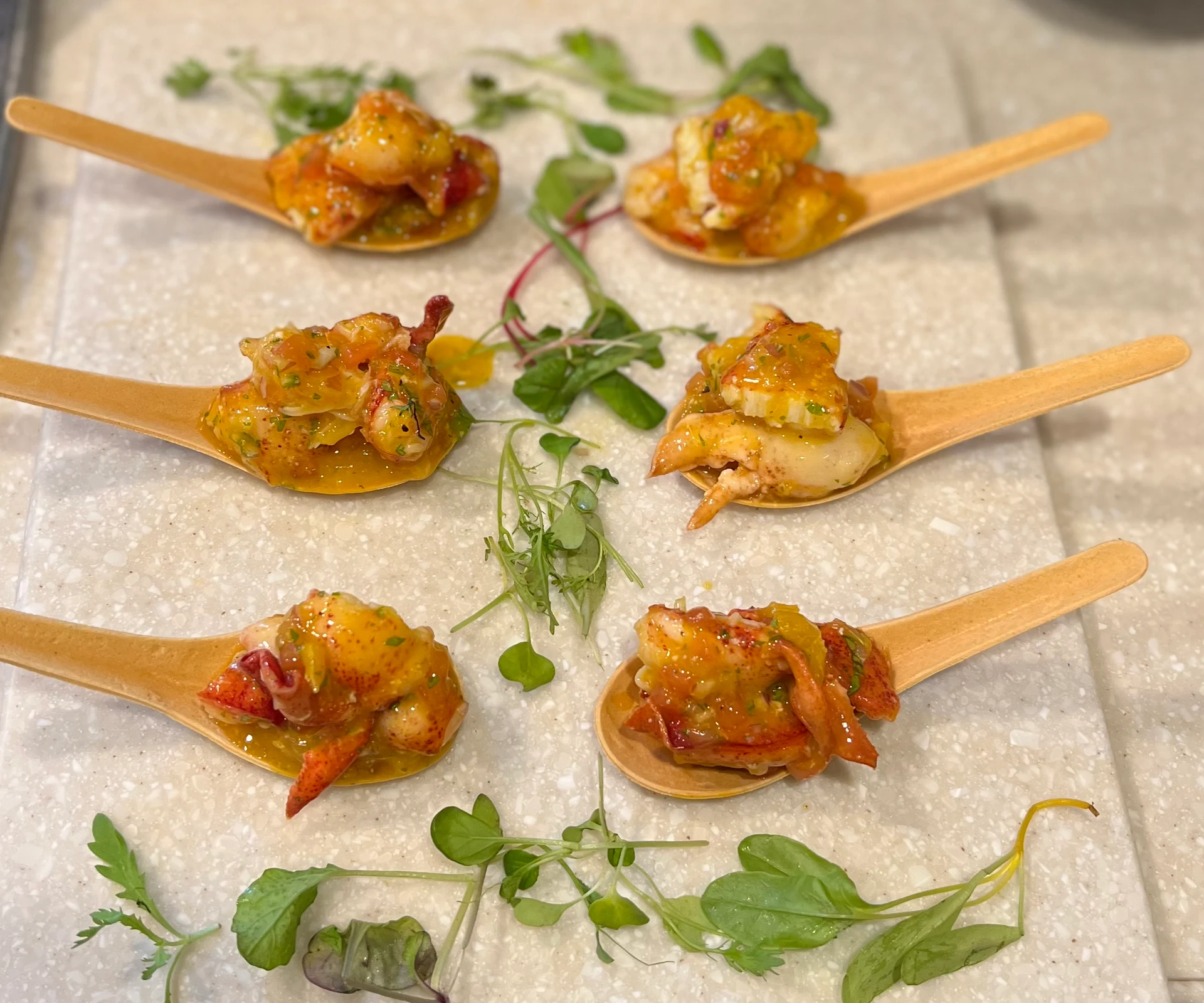 Lobster ceviche appetizers on wooden tasting spoons with microgreens.