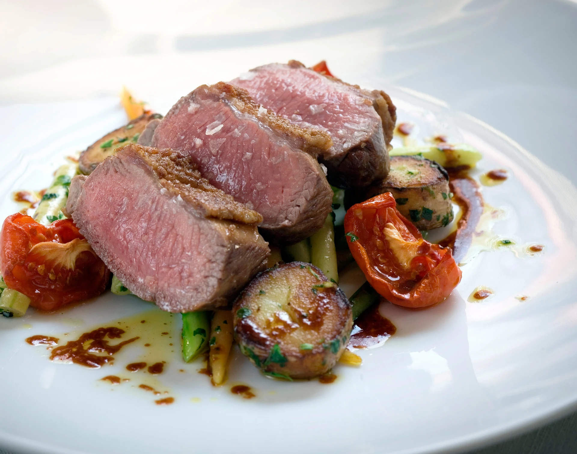 Sliced lamb loin with roasted vegetables and herb sauce.