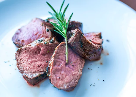 Sliced goat loin garnished with a sprig of rosemary.