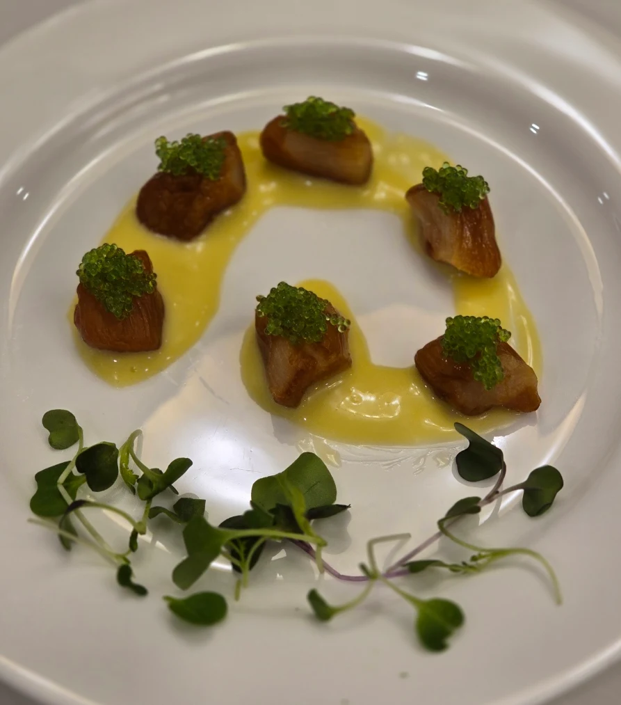 Smoked bay scallops arranged in a circle with green garnish and golden sauce.