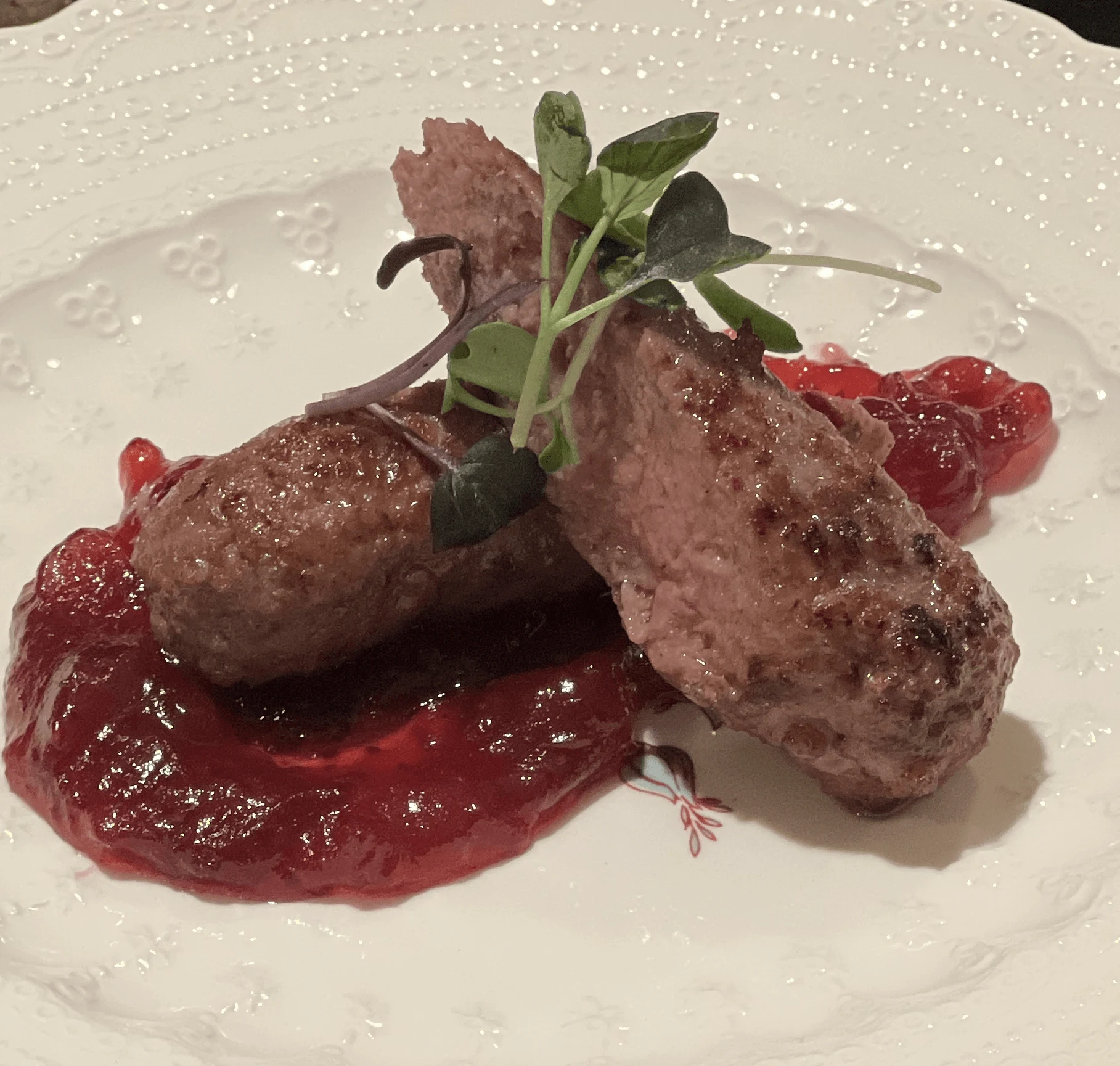 Duck sausage with red fruit sauce and fresh microgreens.