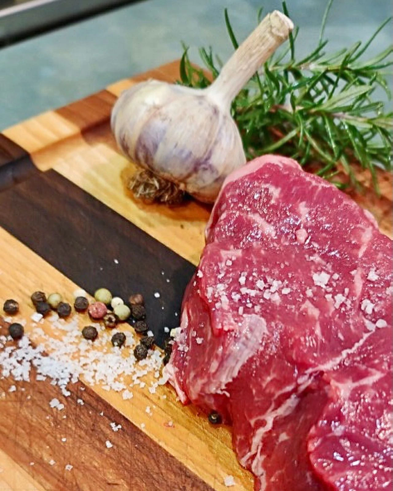 A marbled raw steak on a wooden board with garlic, rosemary and seasonings.