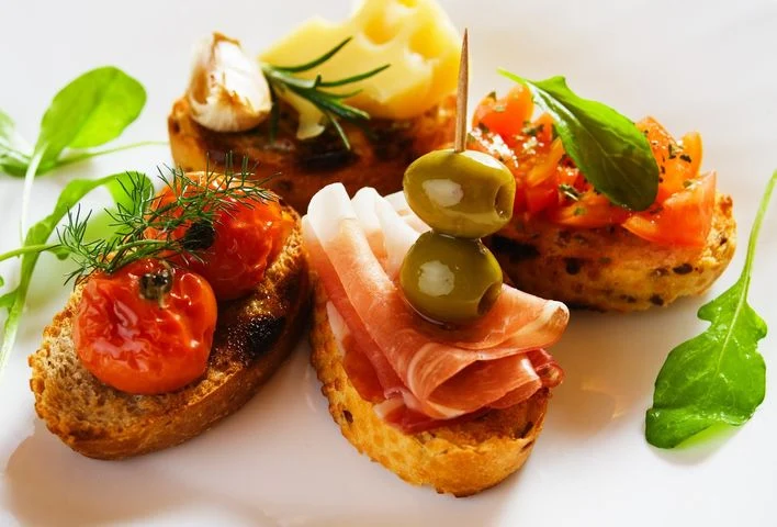 Three crostini topped with tomatoes, cured meat, olives and cheese.