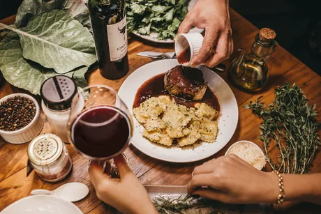 A meal shared with red wine, pasta and fresh herbs at a wooden table.
